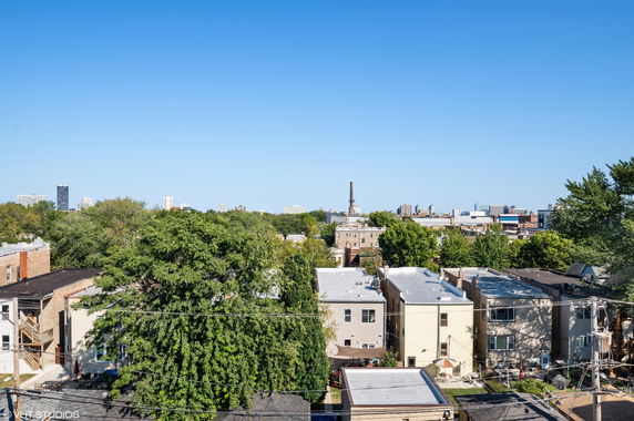 Panoramic view of a residential area with buildings and green trees under a clear blue sky.