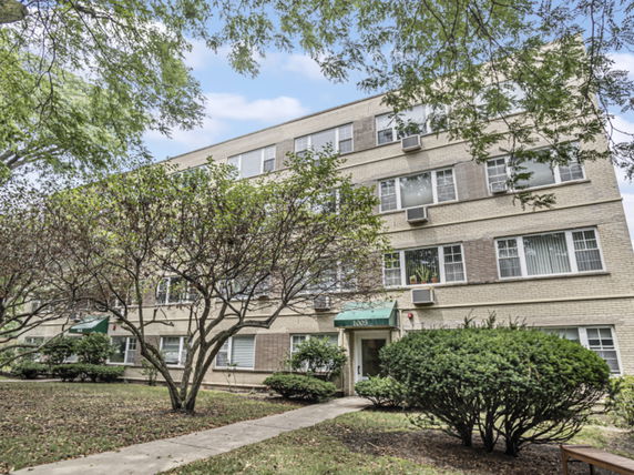Front view of a multi-story residential building with several windows and a green awning over the entrance.