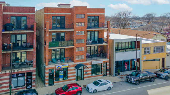 Front view of a multi-story brick building with balconies and commercial spaces at ground level.