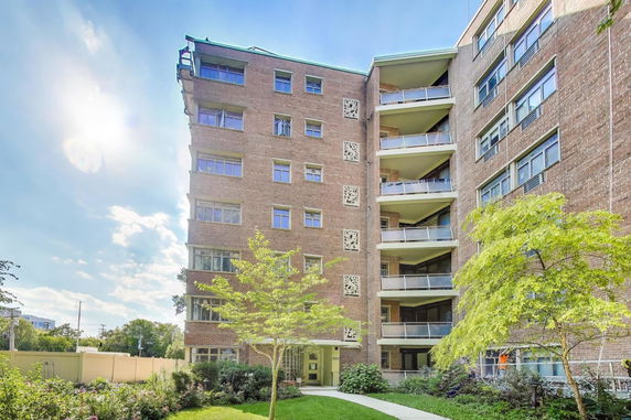 Front view of a multi-story brick apartment building with balconies and decorative panels.