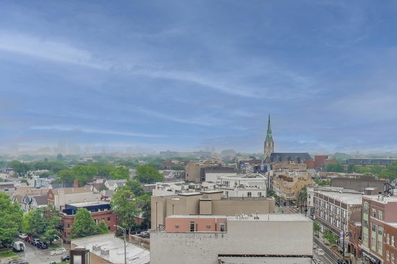 Wide-angle view over a city skyline with diverse buildings and a prominent church steeple.