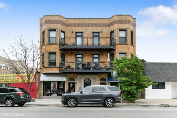 Front view of a three-story brick building with balconies and commercial space on the ground floor.