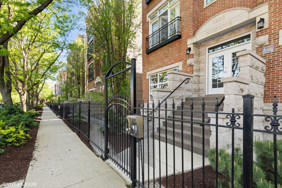 Front view of a multi-story brick building with a black wrought iron fence and entrance steps.