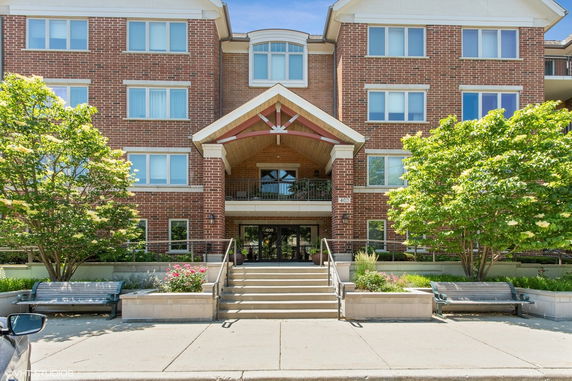 Front view of a multi-story brick building with an entrance canopy and stairs leading to the door.