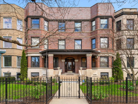 Front view of a brick multi-story residential building with prominent bay windows and a gated entrance.
