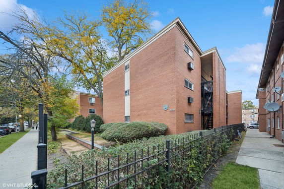 Front view of a multi-story brick apartment building with surrounding trees.
