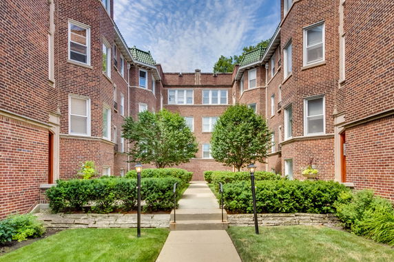 Front view of a multi-story brick building with a landscaped pathway leading to the entrance.
