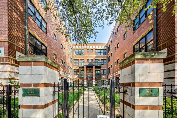 Front view of a multi-story brick apartment building with gated entrance.