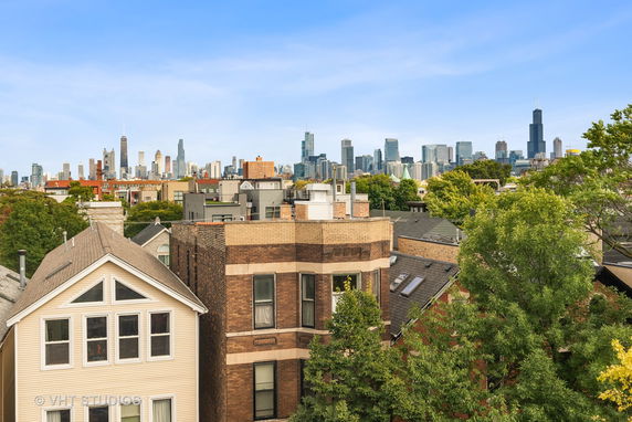 Panoramic view of a city skyline with foreground buildings and trees.