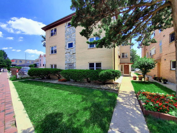 Front view of a multi-story apartment building with beige brickwork and decorative stone elements.