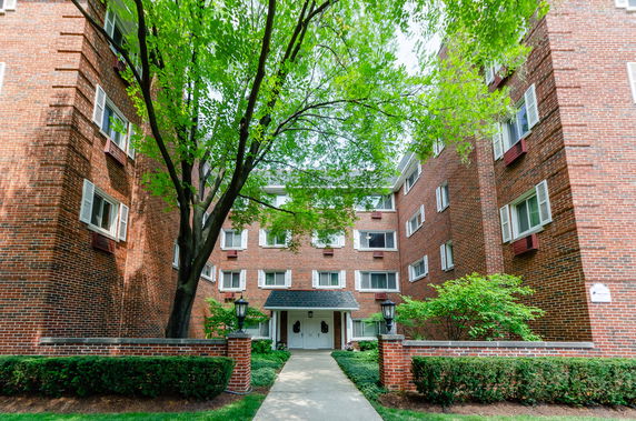 Front view of a multi-story brick apartment building with trees and walkway.