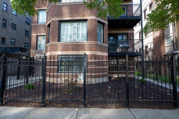 Front view of a multi-story brick building with a wrought iron fence.