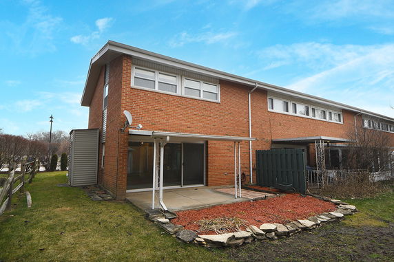 Side view of a two-story brick house with a small patio.
