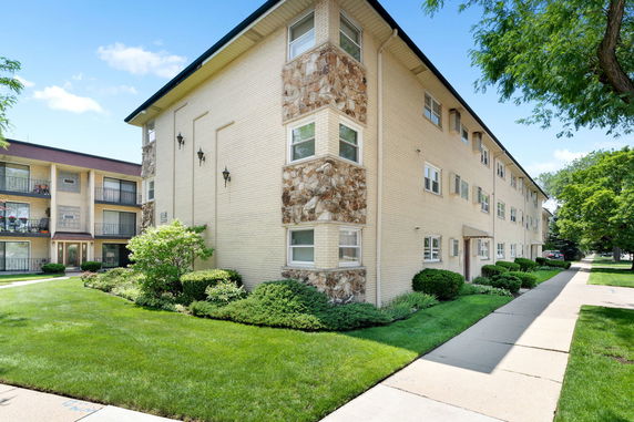 Front view of a multi-story apartment building with a brick exterior and landscaped surroundings.