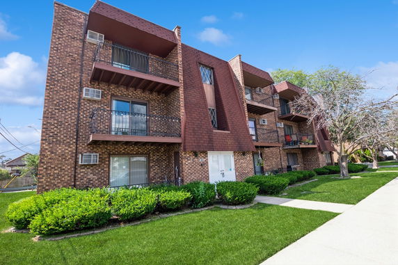 Front view of a multi-story brick apartment building with balconies.