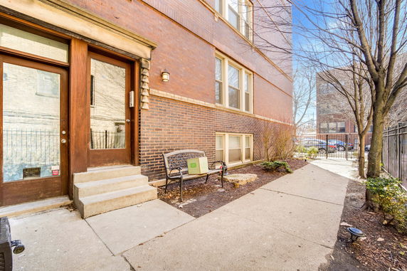Side view of a brick building with a wooden door entrance and small steps, adjacent to a pathway.