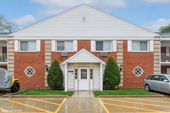 Front view of a two-story brick building with white siding and a central entrance.