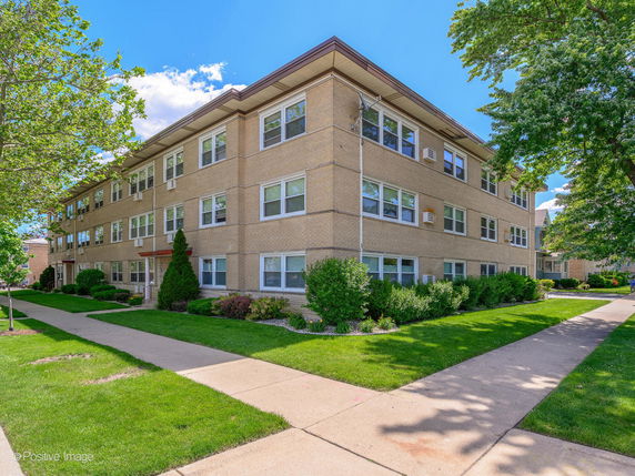 Front view of a three-story apartment building with multiple windows and a walkway.