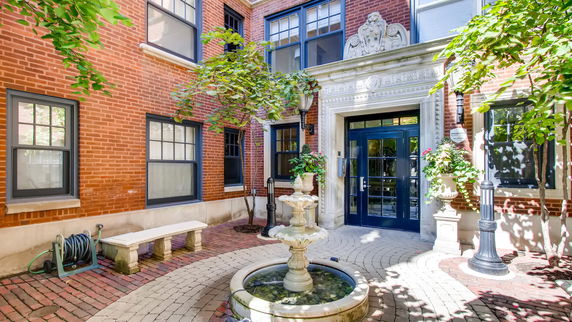 Front view of a brick building entrance with decorative elements and a small fountain.