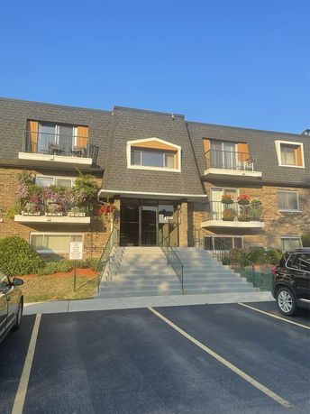 Front view of a multi-story residential building with balconies and a gabled roof.