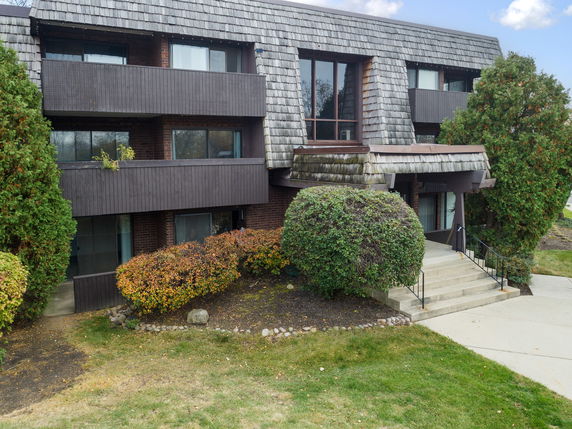 Front view of a multi-story building with balconies and a shingle-style roof.