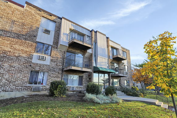 Front view of a three-story brick apartment building with balconies.
