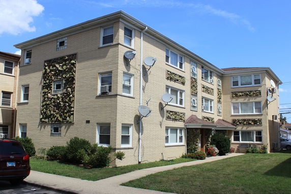 Front view of a three-story brick apartment building with decorative stone panels and multiple satellite dishes.