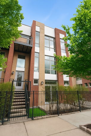 Front view of a modern townhouse with brick and light-colored exterior, featuring large windows and a small balcony.