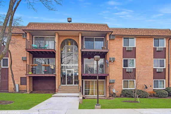 Front view of a three-story brick apartment building with balconies and a central entrance.