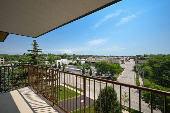 View from a balcony overlooking a street and buildings with trees in the background.