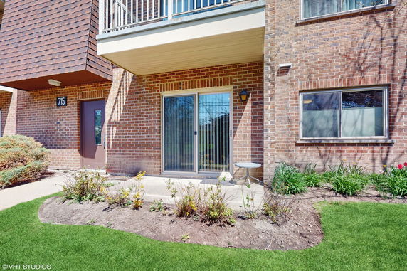 Front view of a brick apartment building entrance with a sliding glass door and a small patio area.