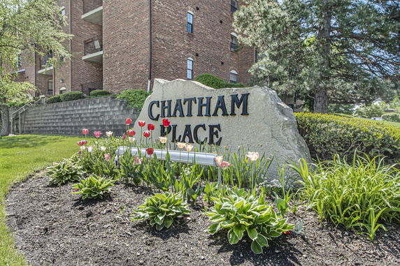 Front view of a multi-story brick building with a garden and signage.