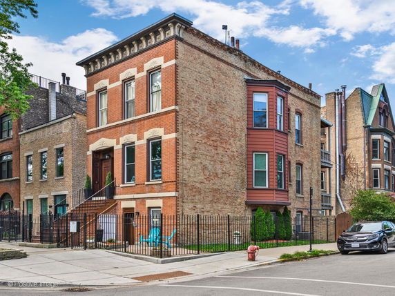Front view of a multi-story brick house with large windows and a fenced yard.