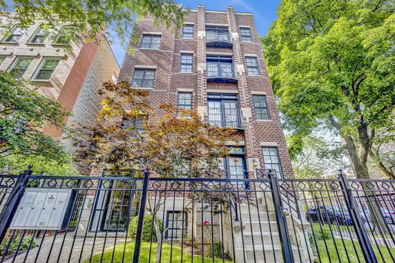 Front view of a multi-story brick building with decorative balconies and a gated entrance.