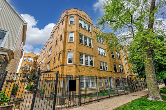 Front view of a multi-story brick building with multiple windows and a gated entrance.