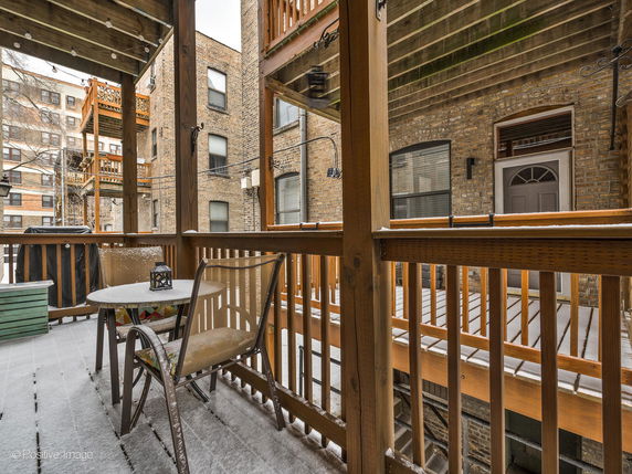 View from a wooden balcony showing brick apartment buildings in a snowy urban environment.