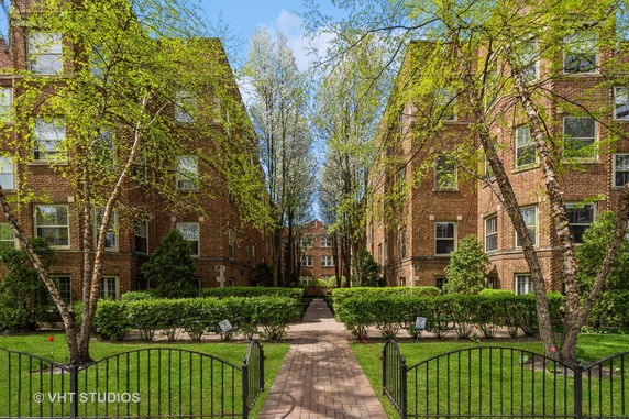 Front view of brick apartment buildings with a central walkway and landscaped greenery.