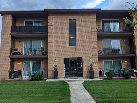 Front view of a three-story brick apartment building with balconies.