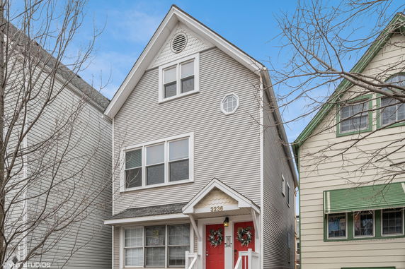Front view of a three-story house with a sharp gable roof and red front doors.