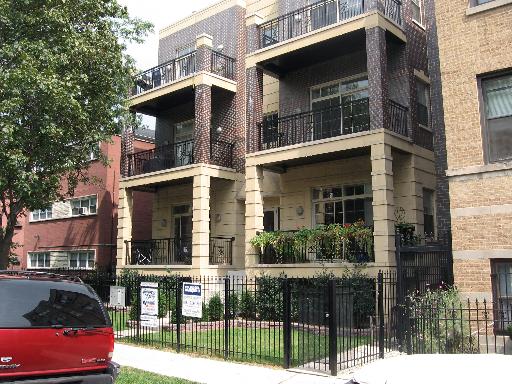 Front view of a multi-story residential building with balconies and a fenced yard.
