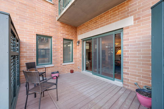 Small outdoor patio area with two chairs, potted plants, and sliding glass doors leading into a room.