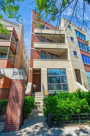 Front view of a multi-story apartment building with balconies and a brick facade.