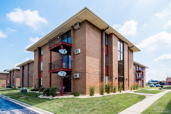 Front view of a multi-story brick apartment building with balconies and satellite dishes.
