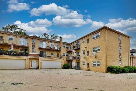 Front view of a brick apartment building with multiple balconies and garage entrances.