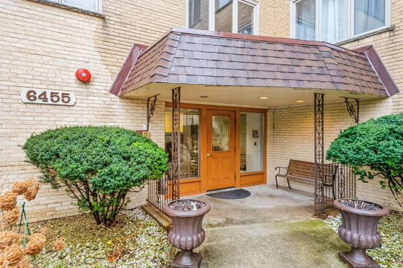 Front entrance of a brick building with canopy and bench.