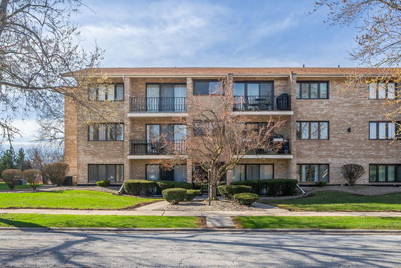Front view of a three-story brick apartment building with balconies.