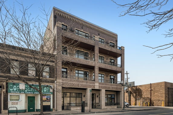 Front view of a multi-story brick building with balconies and ground-floor shops.