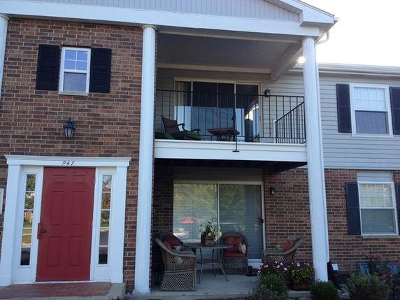 Front view of a two-story brick house with a red door and balcony.