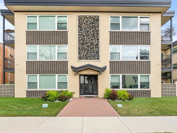 Front view of a multi-story apartment building with a decorative stone panel and numerous windows.