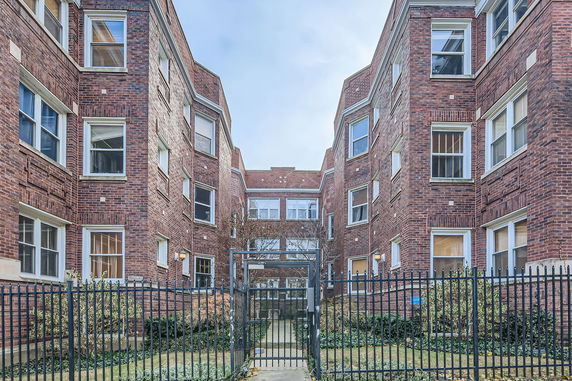 Front view of a multi-story brick residential building with a gated entrance.